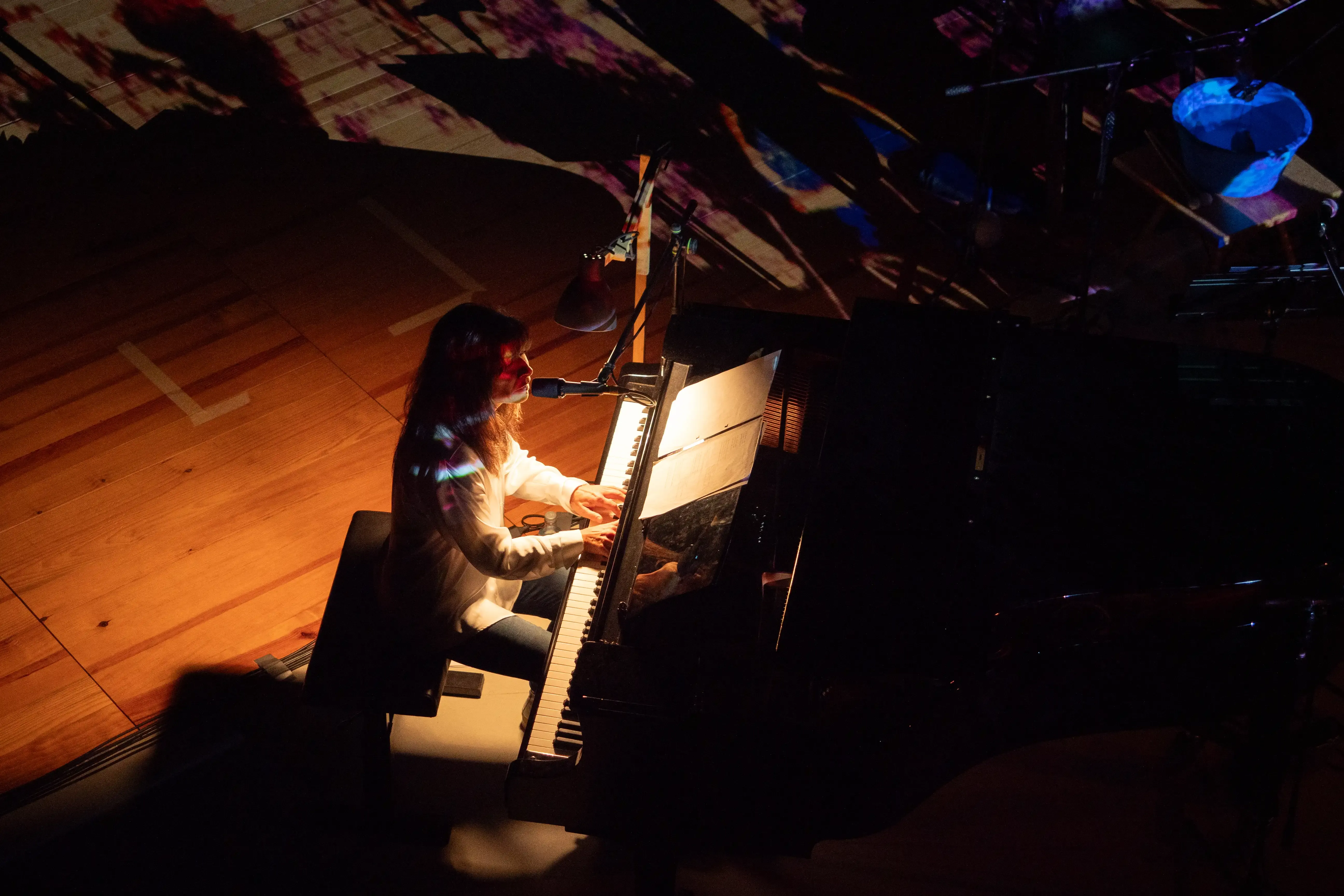 Uma mulher a tocar piano de cauda. Uma projeção cria sombras interessantes no palco.